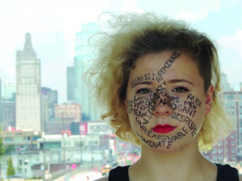 Junior Amber Brownlee sits in front of a view of downtown Kansas City with misconceptions of what feminists are written on her face Sept. 28.  photo by Maddy Medina