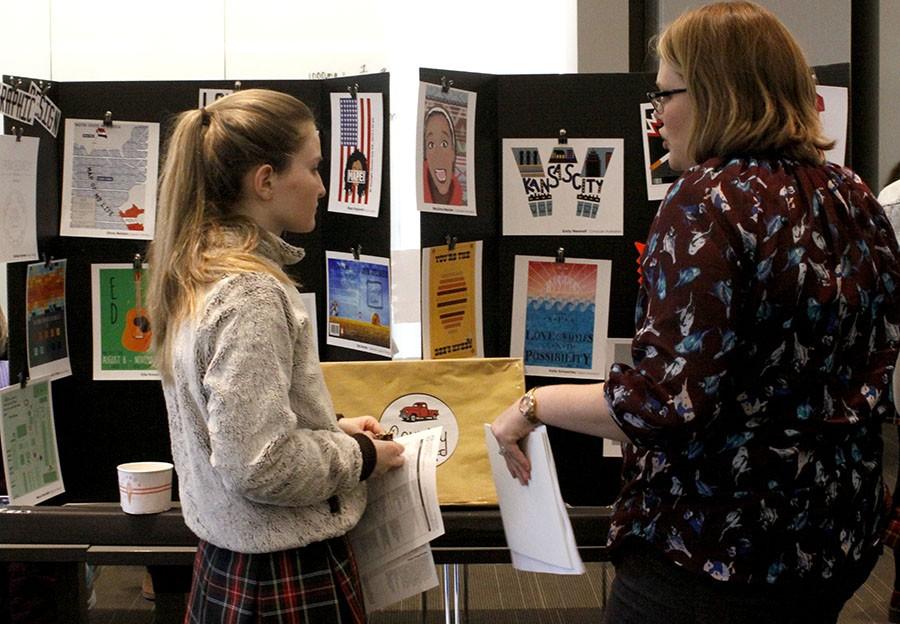 At the first annual STA elective fair on Jan. 12 digital media teacher Kelly Scott explains the courses she offers to junior Katya Blair, such as graphic design and computer illustration and design, using designs created by her previous students. photo by Kate Scofield