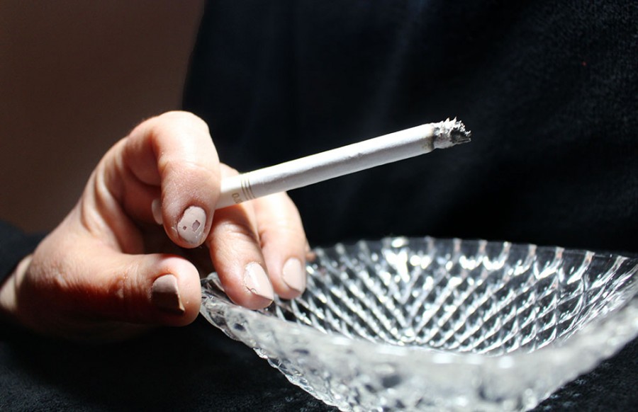 A hand holding a lit cigarette rests on an ash tray. In mid-November, the Kansas City, Mo. City Council and Kansas City, Kan. Unified Government Board of Commission passed an ordinance raising the legal age to buy nicotine and vapor products from 18 years old to 21 years old. photo illustration by Kat Mediavilla