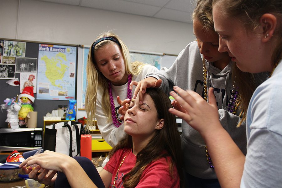 Sophomores Ellie Fuemmeler, from left, Ella Tomasic and Adelle Quick put glitter in Ava Fitzgeralds eyebrows Sept. 21. Many students decorated their faces with gold and purple glitter to fit Fridays theme of Mardi Gras. photo by Amy Schaffer