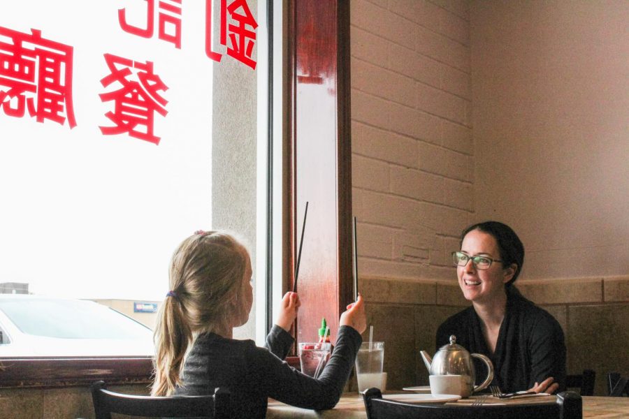 A young girl plays with chopsticks to entertain her mother as they wait for their order.