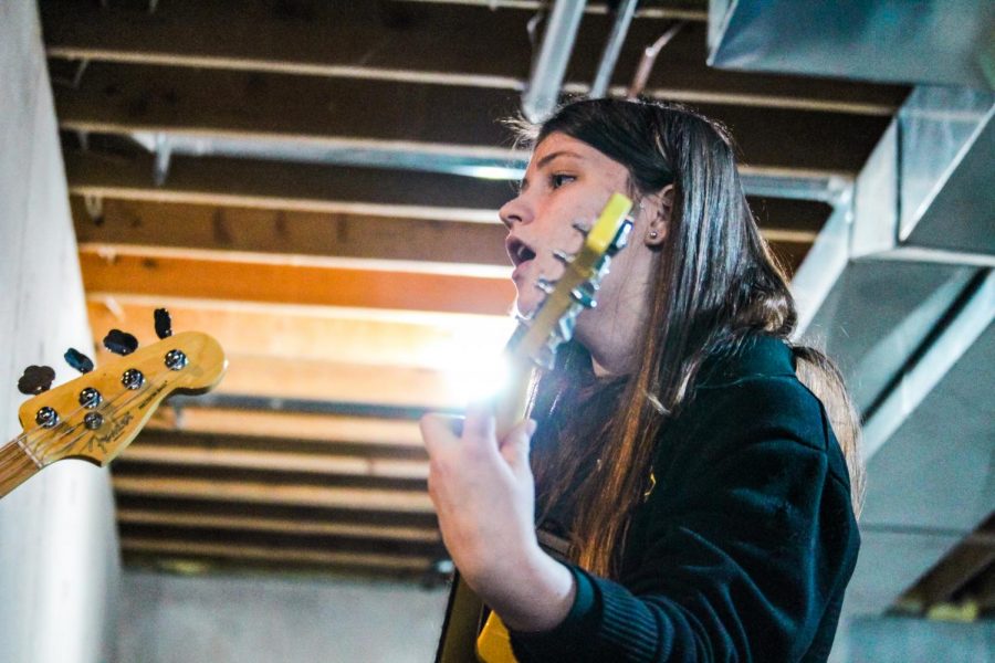 Senior Kylie Schuster sings and plays guitar while practicing with “Yellow House” in her basement Feb. 12. Schuster is the only member of her band to attend STA, so rehearsals are held outside of school. photo by Amy Schaffer