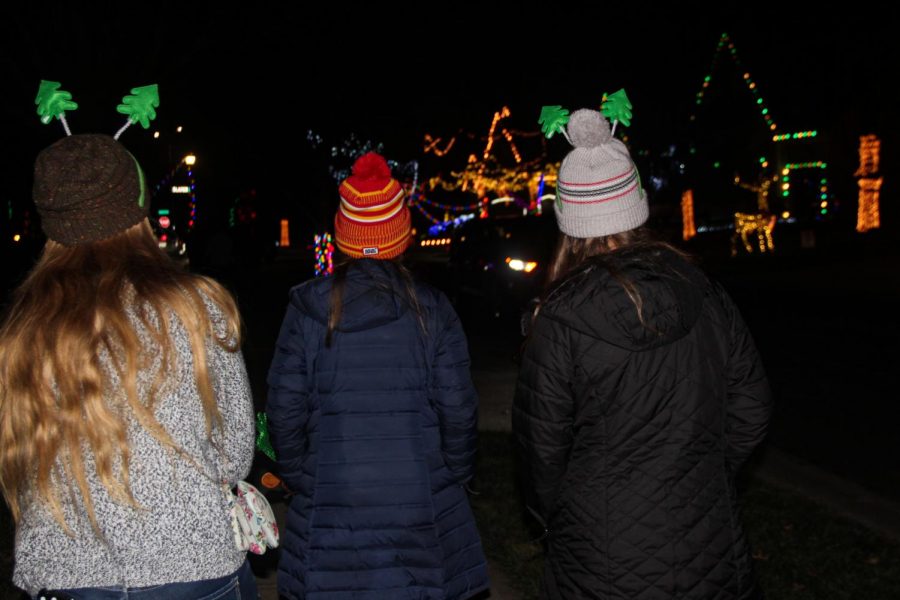 Sophomores, from left, Teresa Elfrink, Stella Hughes and Lucy Doerflinger pause as a car passes in front of a brightly lit house Dec. 13. The street alongside these light displays was packed with cars eager to spend a night of light-watching. photo by Mara Callahan

