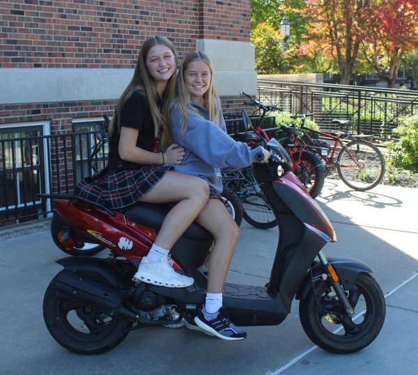 Freshmen Evelyn Batz and Dory Hodes pose on Hodess electric moped. She rides this moped to school almost everyday. photo by Lina Kilgore